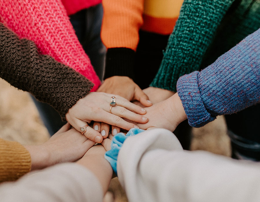 Eine Gruppe junger Menschen mit bunten Kleidern legt die Hände übereinander